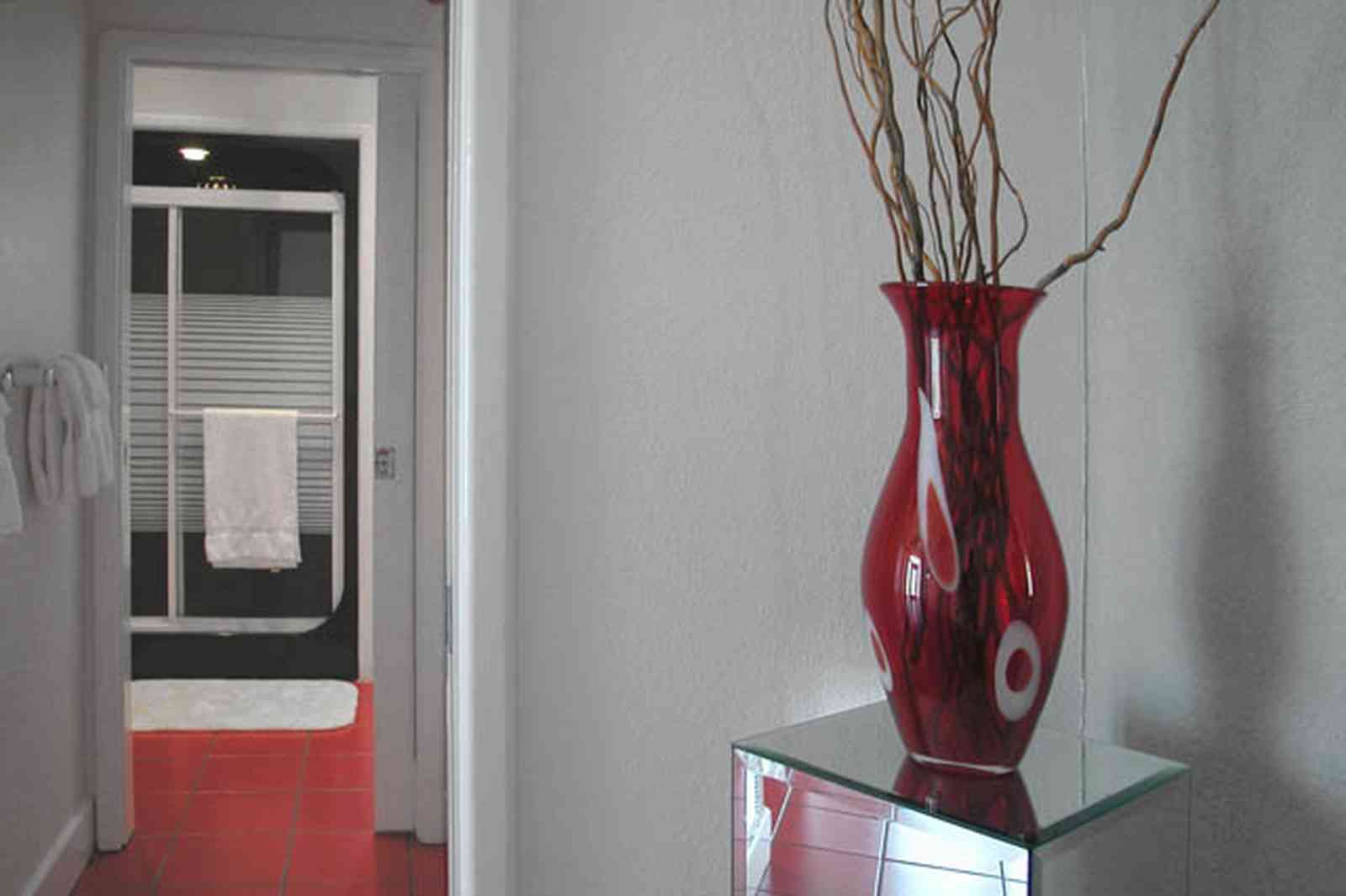 Navarre:-7332-Grand-Navarre-Blvd_30.jpg:  red glass vase, red tile floor, black shower door, art deco decor, mirrored stand