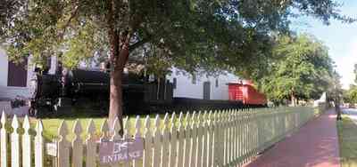 Pensacola:-Historic-Pensacola-Village:-Museum-Of-Industry_02.jpg:  locomotive, caboose, oak tree, picket fence, brick sidewalk