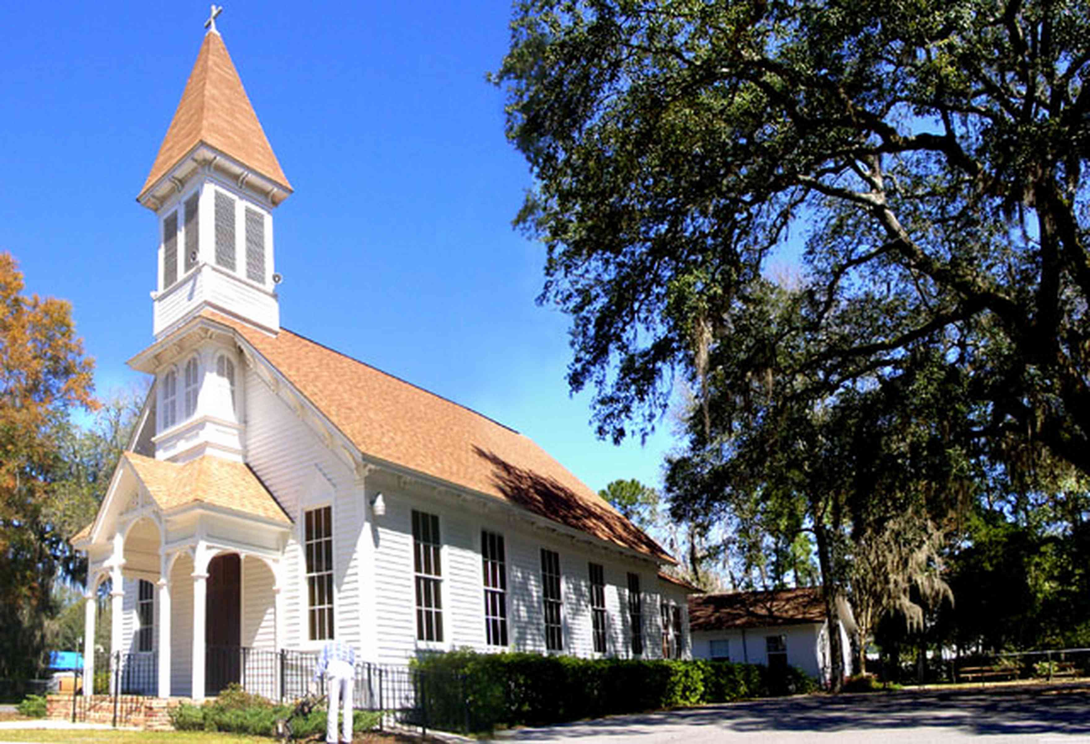 Bagdad:-Methodist-Church_02.jpg:  victorian church, spanish moss, live oak tree, gingerbread trim, gothic revival architectural style, stained glass windows, pointed arch, steep gabled roof, carpenter gothic style