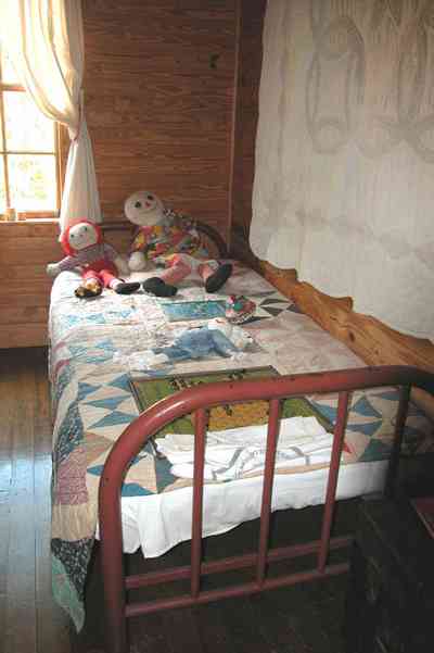 Cantonment:-Roy-Hyatt-Environmental-Center-Dog-Trot-House_10.jpg:  iron bed, quilt, ragdoll, bedroom, wooden walls, wood floor, rocking chair