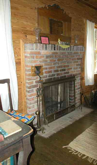 Cantonment:-Roy-Hyatt-Environmental-Center-Dog-Trot-House_15.jpg:  hooked rug, fireplace, desk, iron bed, quilt, ragdoll, bedroom, wooden walls, wood floor, rocking chair