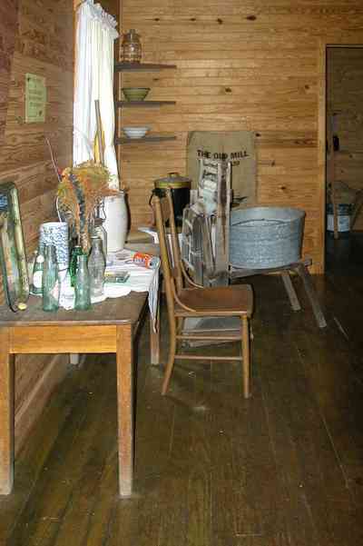 Cantonment:-Roy-Hyatt-Environmental-Center-Dog-Trot-House_18.jpg:  iron bed, quilt, ragdoll, bedroom, wooden walls, wood floor, rocking chair