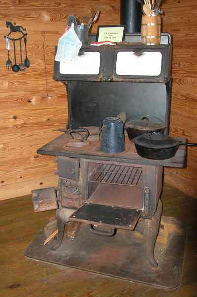 Cantonment:-Roy-Hyatt-Environmental-Center-Dog-Trot-House_19.jpg:  iron bed, quilt, ragdoll, bedroom, wooden walls, wood floor, stove, frying pan, coffee pot, iron, utensils, rocking chair