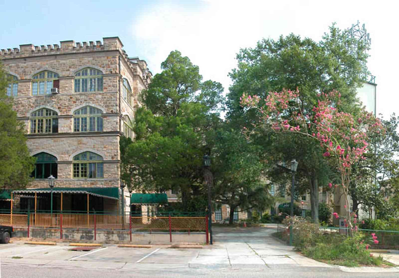 East-Hill:-Tower-East:-Old-Sacred-Heart-Hospital_20.jpg:  crepe myrtle tree, awning, wrought iron fence, pation fir tree, stone facade, battlement, stone courses