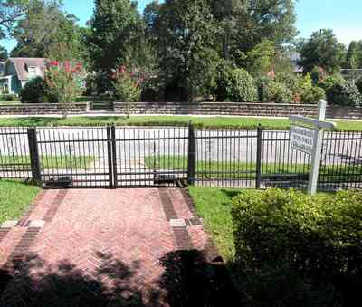 North-Hill:-105-West-Gonzales-Street_02b.jpg:  wrought-iron fence, herringbone brick sidewalk, red brick house, streetscape, crepe myrtle trees, stone wall