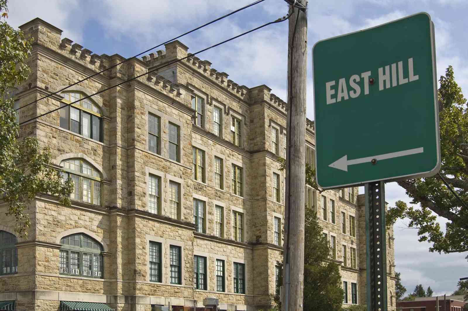 East+Hill_01+WEB.jpg:  sign, historic neighborhood, hospital, romanesque architecture, rough-cut stones, rounded arches, crenelated parapets, 