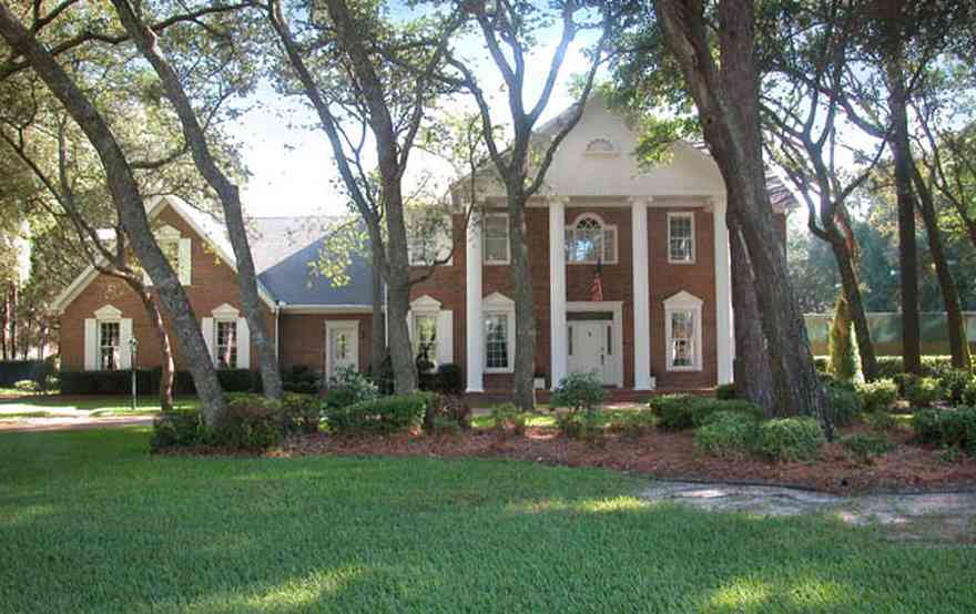 Scenic-Highway:-4450-Devereau-Drive_02.jpg:  colonial architectural style, white columns, shutters, crown molding pediment, circular driveway, carriage lamp, oak trees